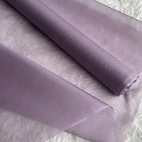 Un rouleau d'Organza de soie multicolore 8 momme au mètre de Longan Craft France est présenté sur une surface texturée blanche, mettant en valeur son luxe diaphane et léger, parfait pour les robes.