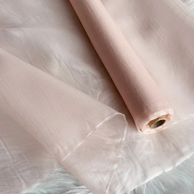 Un rouleau d'Organza de soie multicolore 8 momme au mètre de Longan Craft France, fabriqué à partir de pure soie de mûrier, est partiellement déroulé sur une surface texturée blanche. Ce tissu luxueux est doux, lisse et translucide, idéal pour les robes.