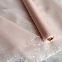 Un rouleau d'Organza de soie multicolore 8 momme au mètre de Longan Craft France, fabriqué à partir de pure soie de mûrier, est partiellement déroulé sur une surface texturée blanche. Ce tissu luxueux est doux, lisse et translucide, idéal pour les robes.