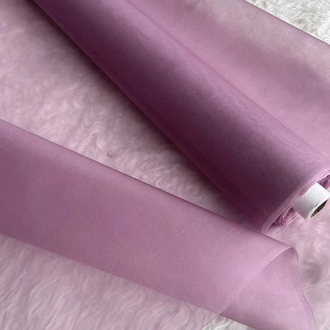 Deux rouleaux d'Organza de soie multicolore 8 momme de Longan Craft France, fabriqués à partir de pure soie de mûrier, sont posés sur une surface blanche et douce. Le luxueux tissu de la robe est violet clair, légèrement translucide et élégant.
