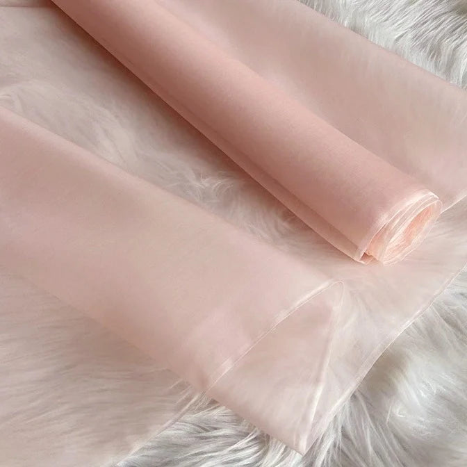 Deux rouleaux de Longan Craft France Organza de soie multicolore 8 momme, en pure soie de mûrier, sont présentés sur une surface blanche. Ce tissu luxueux et translucide a une texture lisse et une brillance élégante, idéale pour les robes.