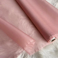 Un rouleau d'Organza de soie multicolore 8 momme au mètre de Longan Craft France, en pure soie de mûrier, est partiellement déroulé sur de la fausse fourrure blanche douce, montrant sa texture lisse et transparente et sa brillance subtile, idéale pour les robes de luxe.