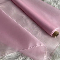 Un rouleau d'"Organza de soie multicolore 8 momme" de Longan Craft France, fabriqué à partir de pure soie de mûrier, est partiellement déroulé sur une surface de fourrure blanche, mettant en valeur sa texture lisse et sa brillance subtile - un tissu de luxe idéal pour les robes.