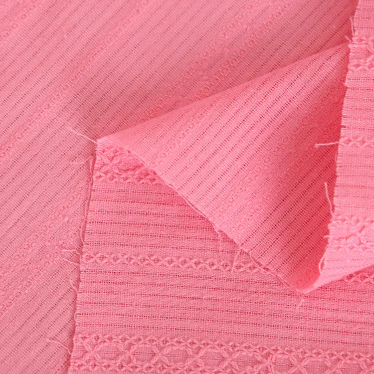 Vue détaillée du tissu dobby coton multicolore au mètre de Longan Craft France, montrant des rayures texturées et des broderies en rose, avec un coin plié pour révéler l'envers - le textile idéal pour des chemises confortables.