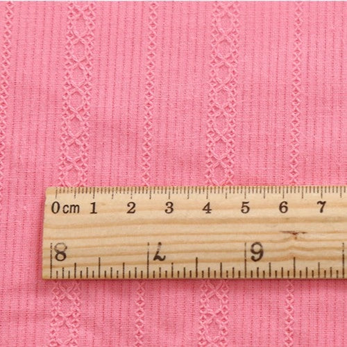 Une règle en bois marque les centimètres sur Tissu dobby coton multicolore au mètre de Longan Craft France, a tissu dobby texturé à rayures, parfait et confortable pour chemises et vêtements.