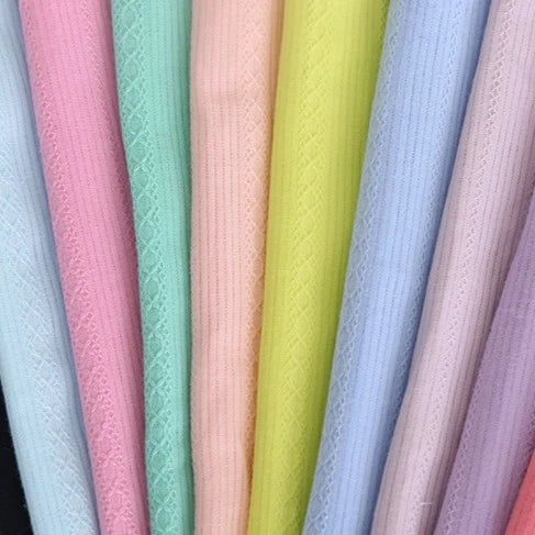 Des rangées de tissu dobby coton multicolore au mètre de Longan Craft France sont suspendues verticalement dans des tons pastel - bleu clair, rose, vert, pêche, jaune, lavande et violet - avec des rayures texturées ; idéal pour des chemises confortables.