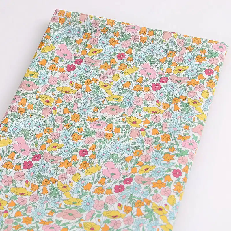 Le Tissu linon de coton léger au mètre de Longan Craft France présente un imprimé floral multicolore avec des fleurs roses, jaunes, orange et rouges ainsi que des feuilles vertes sur fond blanc - parfait pour les vêtements d'été.
