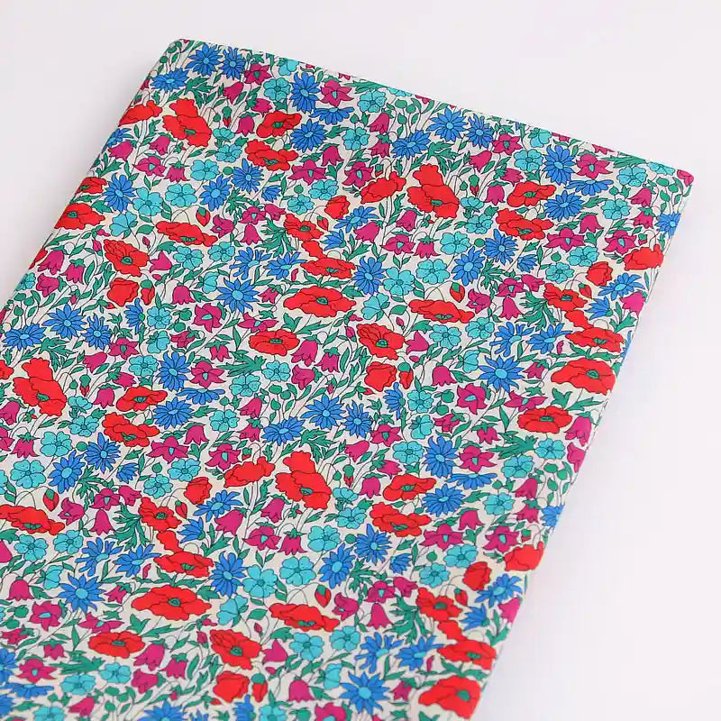 Longan Craft France présente un tissu linon de coton léger au mètre, imprimé floral multicolore (rouge, bleu, violet et vert sur fond blanc), idéal pour la confection de vêtements d'été. Le tissu est soigneusement plié sur une surface blanche.