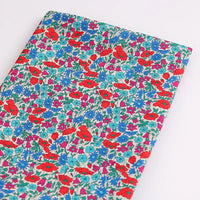Longan Craft France présente un tissu linon de coton léger au mètre, imprimé floral multicolore (rouge, bleu, violet et vert sur fond blanc), idéal pour la confection de vêtements d'été. Le tissu est soigneusement plié sur une surface blanche.
