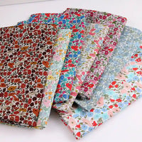 Six pièces pliées du tissu linon de coton léger au mètre de Longan Craft France, aux imprimés floraux multicolores, sont disposées en éventail, idéal pour les vêtements d'été. Chaque tissu présente des motifs rouges, bleus, roses et verts sur des fonds variés.