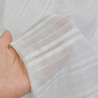 Une main tend le tissu dobby leno multicolore au mètre de Longan Craft France, une matière jacquard dobby coton ajourée à rayures texturées, semi-transparente, parfaite pour robes et vêtements légers.