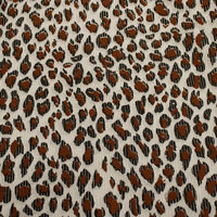 Gros plan sur le tissu côtelé imprimé léopard multicolore au mètre de Longan Craft France, un velours de polyester doux à l'imprimé animalier, avec des taches brunes et noires irrégulières sur un fond beige clair, idéal pour l'habillement.
