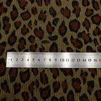 Une règle métallique Longan Craft France, indiquant les centimètres 0-13, repose sur leur tissu côtelé imprimé léopard multicolore au mètre : un velours côtelé polyester avec un motif animalier doux, marron, noir et beige pour l'habillement.