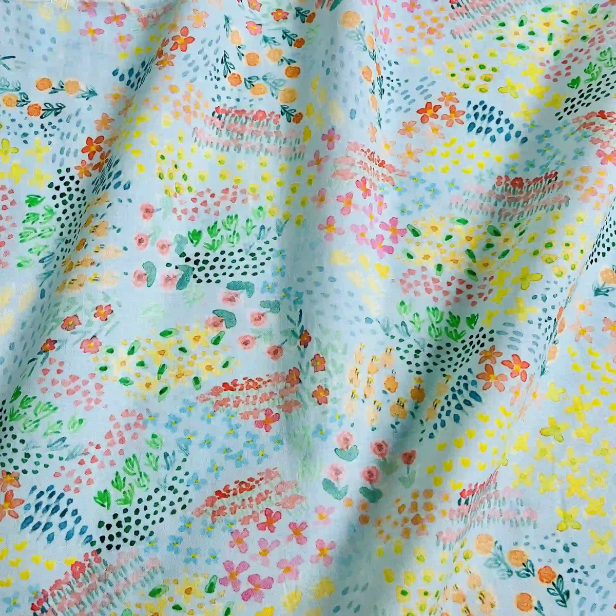 Un gros plan de Linon de coton imprimé multicolore au mètre par Longan Craft France montre son tissu linon de coton à fleurs bleu clair, légèrement froissé, présentant des motifs floraux abstraits pastel avec des points et des lignes.