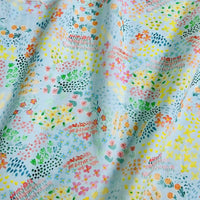 Un gros plan de Linon de coton imprimé multicolore au mètre par Longan Craft France montre son tissu linon de coton à fleurs bleu clair, légèrement froissé, présentant des motifs floraux abstraits pastel avec des points et des lignes.