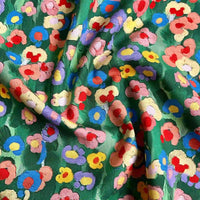 Un gros plan du Linon de coton imprimé multicolore au mètre de Longan Craft France montre son coton vert doux et légèrement froissé avec un imprimé floral coloré, comprenant des fleurs rouges, roses, bleues et jaunes qui créent des reflets lumineux variés.