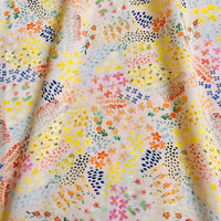 Un gros plan de Linon de coton imprimé multicolore par Longan Craft France montre un tissu de coton doux à motifs floraux en jaune, rose, orange, bleu et vert sur un fond pâle avec des plis visibles.