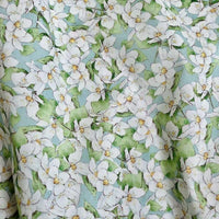 Un gros plan du Linon de coton imprimé multicolore au mètre par Longan Craft France montre des fleurs blanches avec des centres jaunes et des feuilles vertes sur un fond bleu clair, créant un charmant motif floral sur ce linon en tissu de coton doux.