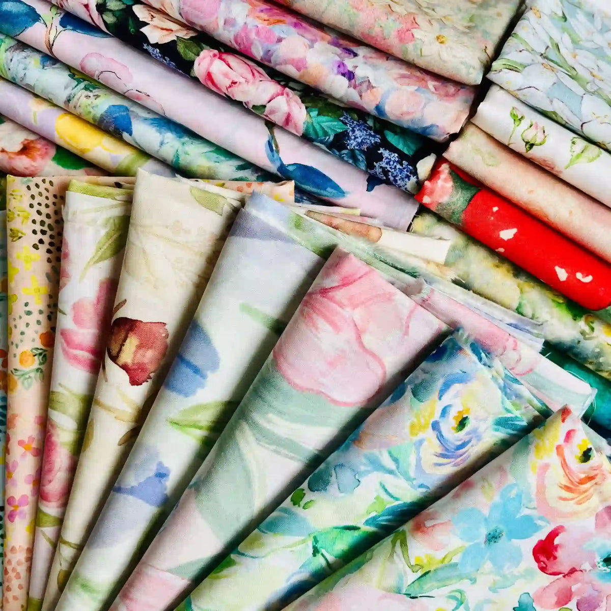 Linon de coton imprimé multicolore au mètre de Longan Craft France, un tissu floral doux, est présenté plié et empilé, mettant en valeur ses motifs floraux pastels et vibrants.