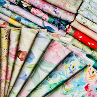 Linon de coton imprimé multicolore au mètre de Longan Craft France, un tissu floral doux, est présenté plié et empilé, mettant en valeur ses motifs floraux pastels et vibrants.