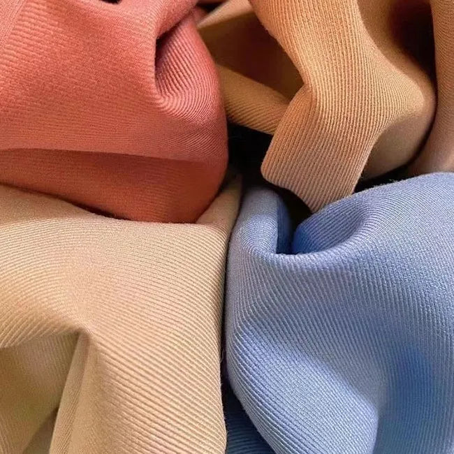 Un gros plan de la gabardine stretch multicolore au mètre de Longan Craft France montre sa texture douce et finement côtelée et sa surface lisse en viscose, dans des tons rose, beige et bleu pastel, idéaux pour les uniformes personnalisés.