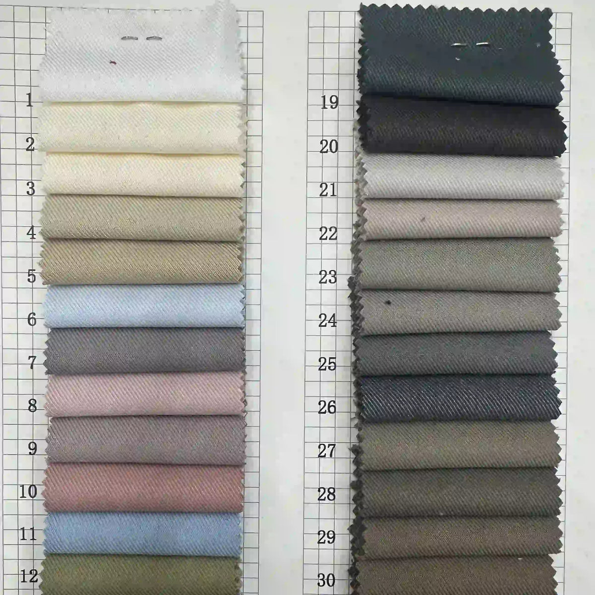 Deux colonnes verticales d'échantillons de tissu en viscose gabardine numérotés en blanc, beige, gris, marron, bleu et rose sont présentées sur une grille ; chacune est attachée en haut. Produit : Tissu gabardine stretch multicolore par Longan Craft France.