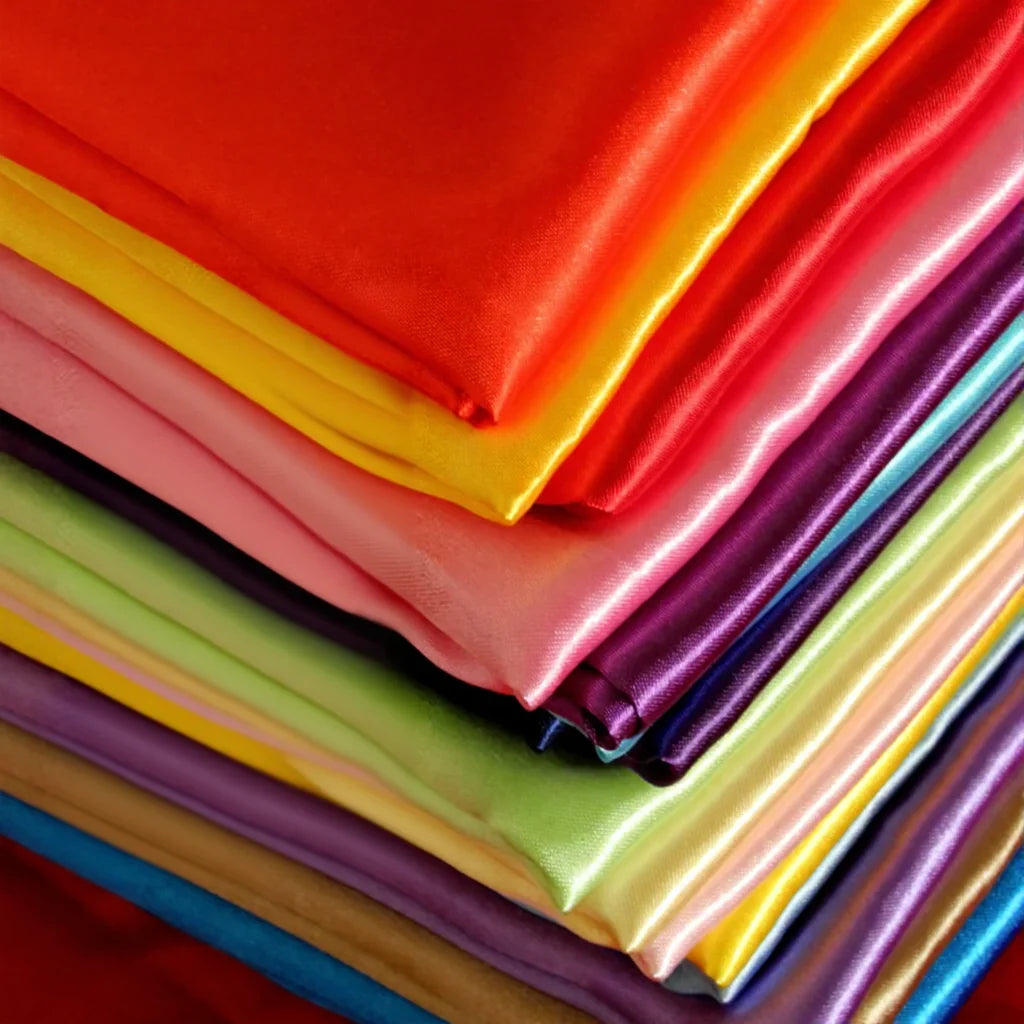 Un gros plan de Tissu en satin multicolore au mètre de Longan Craft France montre un tissu de polyester satiné brillant, soigneusement empilé, dans des couleurs unies vives, idéal pour la confection de vêtements et de robes.