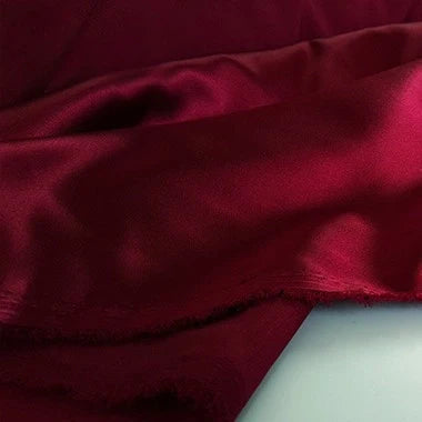 Un gros plan du tissu en satin multicolore au mètre de Longan Craft France, un satin de polyester lisse et brillant idéal pour l'habillement, montre sa texture douce et son bord légèrement effiloché.