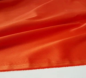 Un gros plan du tissu en satin multicolore au mètre de Longan Craft France montre un polyester lisse et brillant avec un bord cousu visible, idéal pour les vêtements et disponible au mètre.