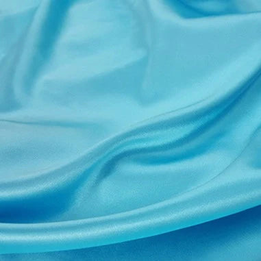 Gros plan sur un tissu en satin bleu clair, lisse et brillant, de Longan Craft France, un tissu en satin de polyester multicolore idéal pour l'habillement, montrant de légers plis et de douces rides sur sa surface.