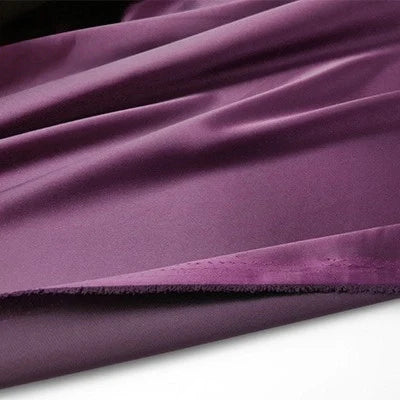 Un morceau de Tissu en satin multicolore au mètre de Longan Craft France, un satin de polyester soyeux idéal pour l'habillement, est disposé avec de légers plis et un bord brut visible sur le bas.