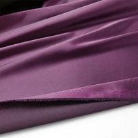 Un morceau de Tissu en satin multicolore au mètre de Longan Craft France, un satin de polyester soyeux idéal pour l'habillement, est disposé avec de légers plis et un bord brut visible sur le bas.