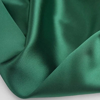 Un gros plan du Tissu en satin multicolore au mètre, lisse et vert foncé, de Longan Craft France, montre des plis de polyester brillants, idéaux pour créer des vêtements élégants.