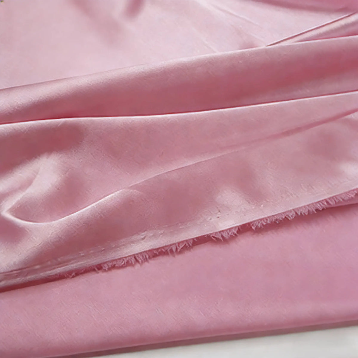 Gros plan sur le tissu satin polyester multicolore au mètre de Longan Craft France, qui présente un éclat doux et une texture délicate, avec de légers plis et des bords effilochés - idéal pour les vêtements.