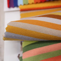 Un gros plan du Tissu French Terry coton à rayures multicolores au mètre de Longan Craft France met en évidence ses rayures jaunes, blanches et grises vibrantes, idéales pour créer des sweatshirts uniques et chauds avec ce tissu tricoté extensible.