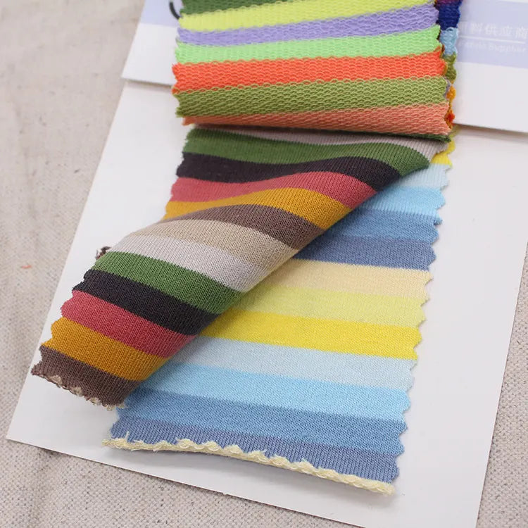 Une carte d'échantillons montre des échantillons du tissu French Terry coton à rayures multicolores au mètre de Longan Craft France - un tissu de sweat-shirt en maille extensible - en bleu, jaune, vert, rouge et marron sur fond blanc. Idéal pour découvrir des motifs uniques.