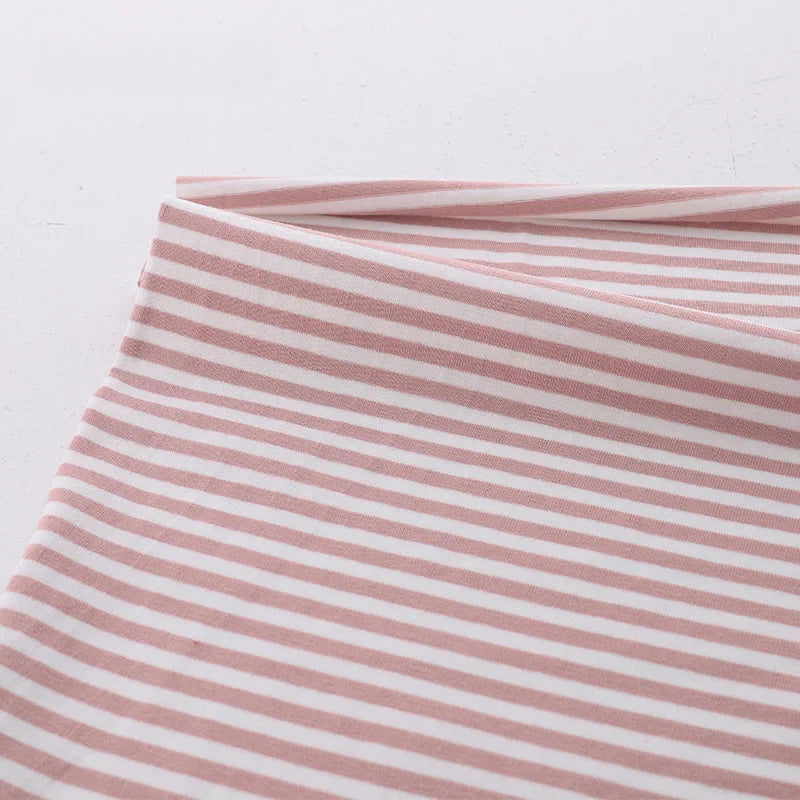 Gros plan sur un pliage de Longan Craft France tissu jersey coton rayé multicolore au mètre, un tissu doux et extensible en coton-elasthanne avec des rayures horizontales roses et blanches, présenté sur un fond clair uni.