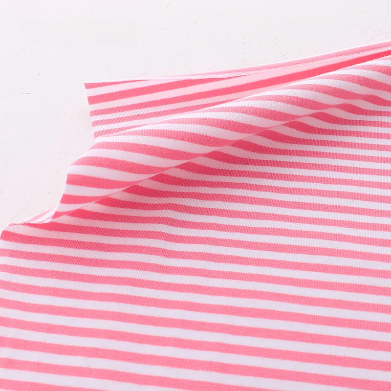 Le tissu jersey coton rayé multicolore Longan Craft France, vendu au mètre et extensible, est présenté sur une surface blanche avec un coin relevé pour mettre en valeur sa texture idéale pour vêtements de sport.