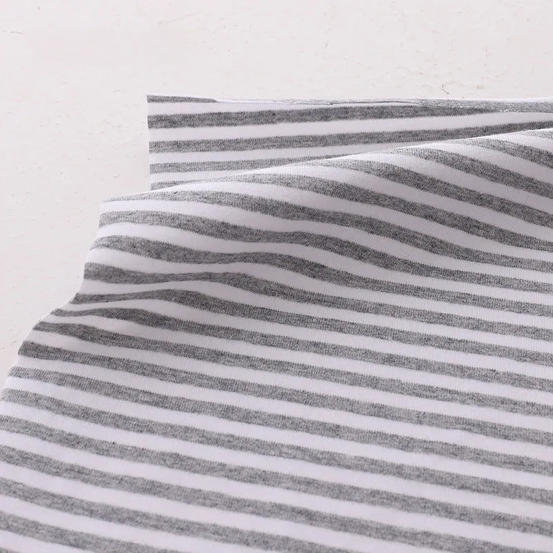 Gros plan sur le Tissu jersey coton rayé multicolore au mètre de Longan Craft France, un jersey coton élasthanne extensible pour vêtements de sport, montrant des rayures horizontales blanches et grises avec de légers plis sur un fond clair.
