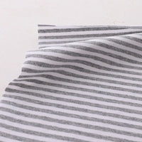 Gros plan sur le Tissu jersey coton rayé multicolore au mètre de Longan Craft France, un jersey coton élasthanne extensible pour vêtements de sport, montrant des rayures horizontales blanches et grises avec de légers plis sur un fond clair.