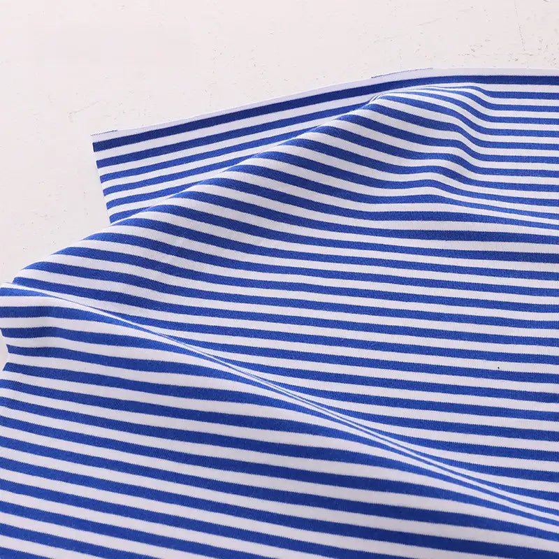 The Longan Craft France Tissu jersey coton rayé multicolore au mètre, un jersey coton élasthanne extensible pour vêtements de sport, présente des rayures horizontales bleues et blanches sur fond uni blanc.