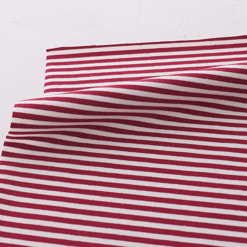 Un morceau de tissu Longan Craft France jersey coton rayé multicolore au mètre, extensible et idéal pour vêtements de sport, est posé à plat avec une pliure centrale, créant une légère ombre sur un fond clair.