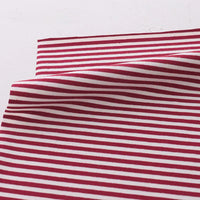 Un morceau de tissu Longan Craft France jersey coton rayé multicolore au mètre, extensible et idéal pour vêtements de sport, est posé à plat avec une pliure centrale, créant une légère ombre sur un fond clair.