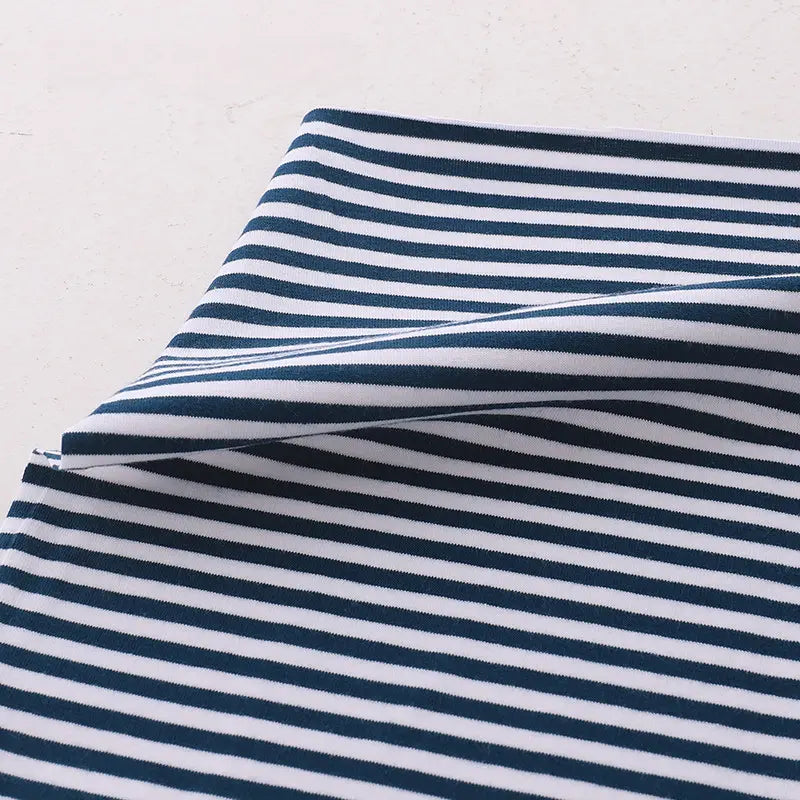 Gros plan sur le tissu jersey coton rayé multicolore au mètre de Longan Craft France, un tissu jersey de coton extensible pour vêtements de sport, avec des rayures horizontales bleu marine et blanches, soigneusement plié sur une surface claire.