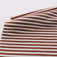 Gros plan sur le tissu jersey coton rayé multicolore au mètre de Longan Craft France, un tissu jersey de coton extensible pour vêtements de sport, avec des rayures marron et blanches et une fermeture éclair le long du bord supérieur sur une surface claire.