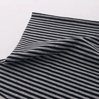 Un morceau de Tissu jersey coton rayé multicolore au mètre de Longan Craft France, jersey coton élasthanne extensible pour vêtements de sport, présente des rayures horizontales noires et gris clair et repose sur une surface blanche avec un pli.