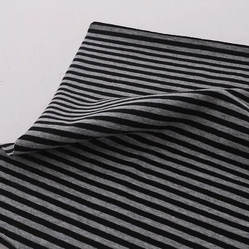 Un morceau de "Tissu jersey coton rayé multicolore au mètre" de Longan Craft France, un tissu extensible en jersey de coton pour vêtements de sport, est présenté à plat avec un coin plié sur une surface blanche.