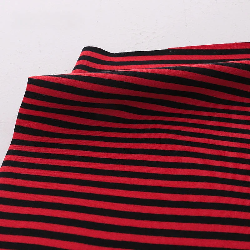 Un morceau de Tissu jersey coton rayé multicolore au mètre de Longan Craft France, un jersey de coton extensible pour vêtements de sport, avec des rayures horizontales noires et rouges régulièrement espacées, est posé sur une surface blanche et légèrement plié dans le coin supérieur gauche.