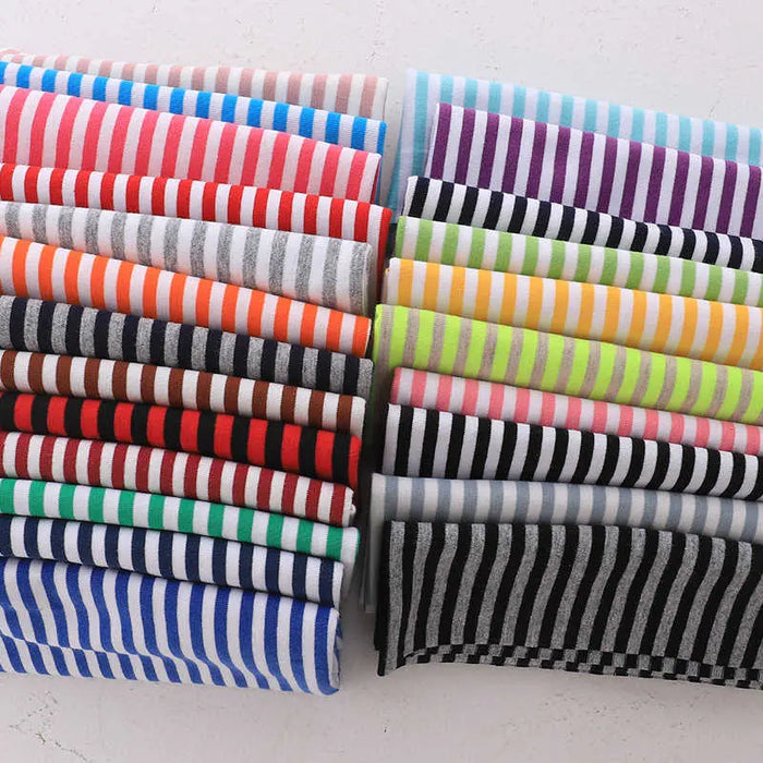 Une sélection de Tissu jersey coton rayé multicolore au mètre de Longan Craft France est soigneusement disposée en rangées, montrant des bandes horizontales rouges, orange, vertes, bleues, violettes, noires, blanches et grises sur une surface blanche.