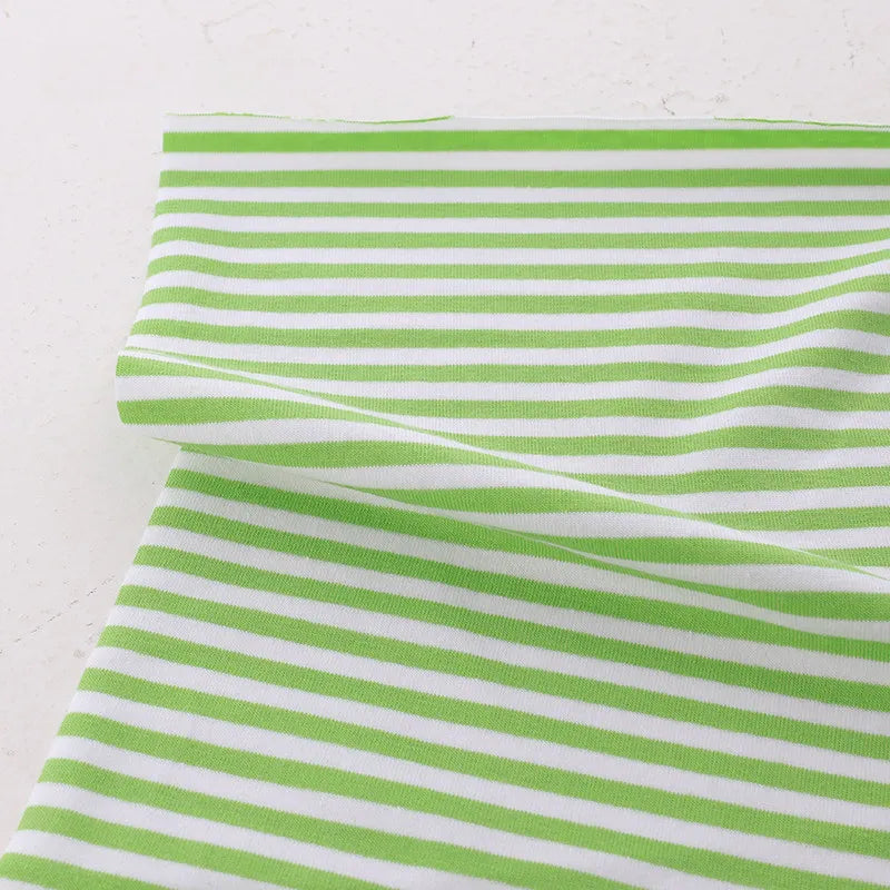 The Tissu jersey coton rayé multicolore de Longan Craft France, un jersey coton élasthanne extensible pour vêtements de sport, est présenté à plat sur une surface claire avec une section légèrement pliée.